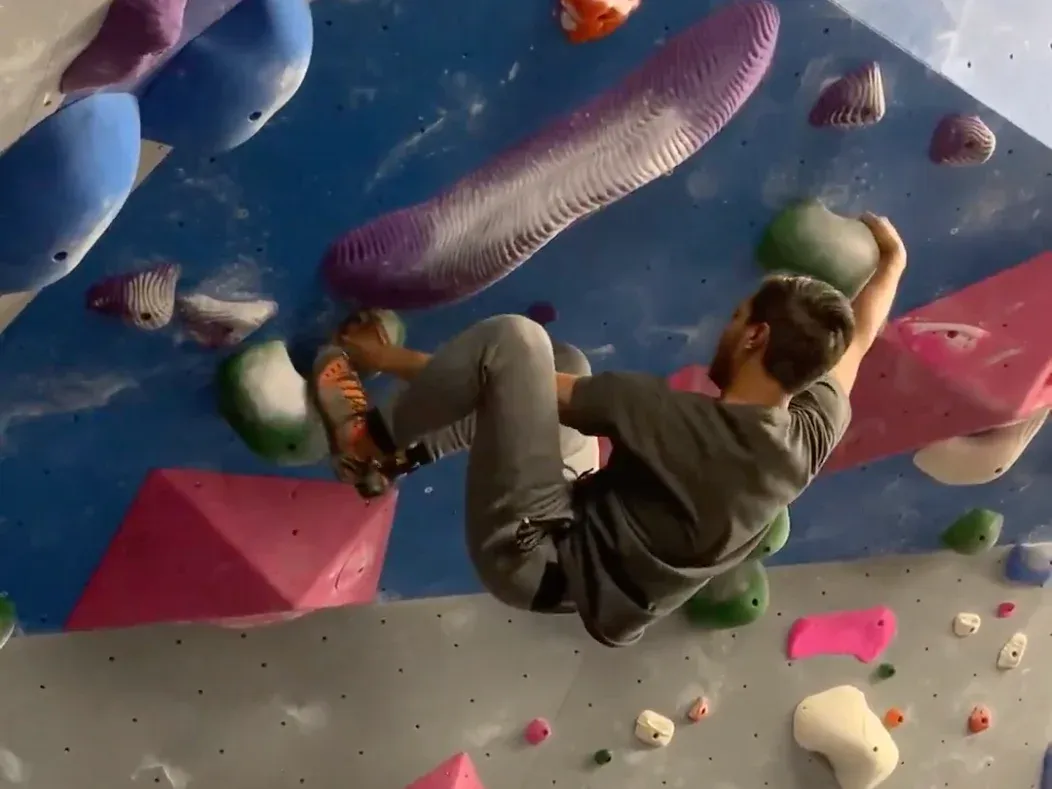 Me climbing an overhanging indoor bouldering wall with colorful holds.